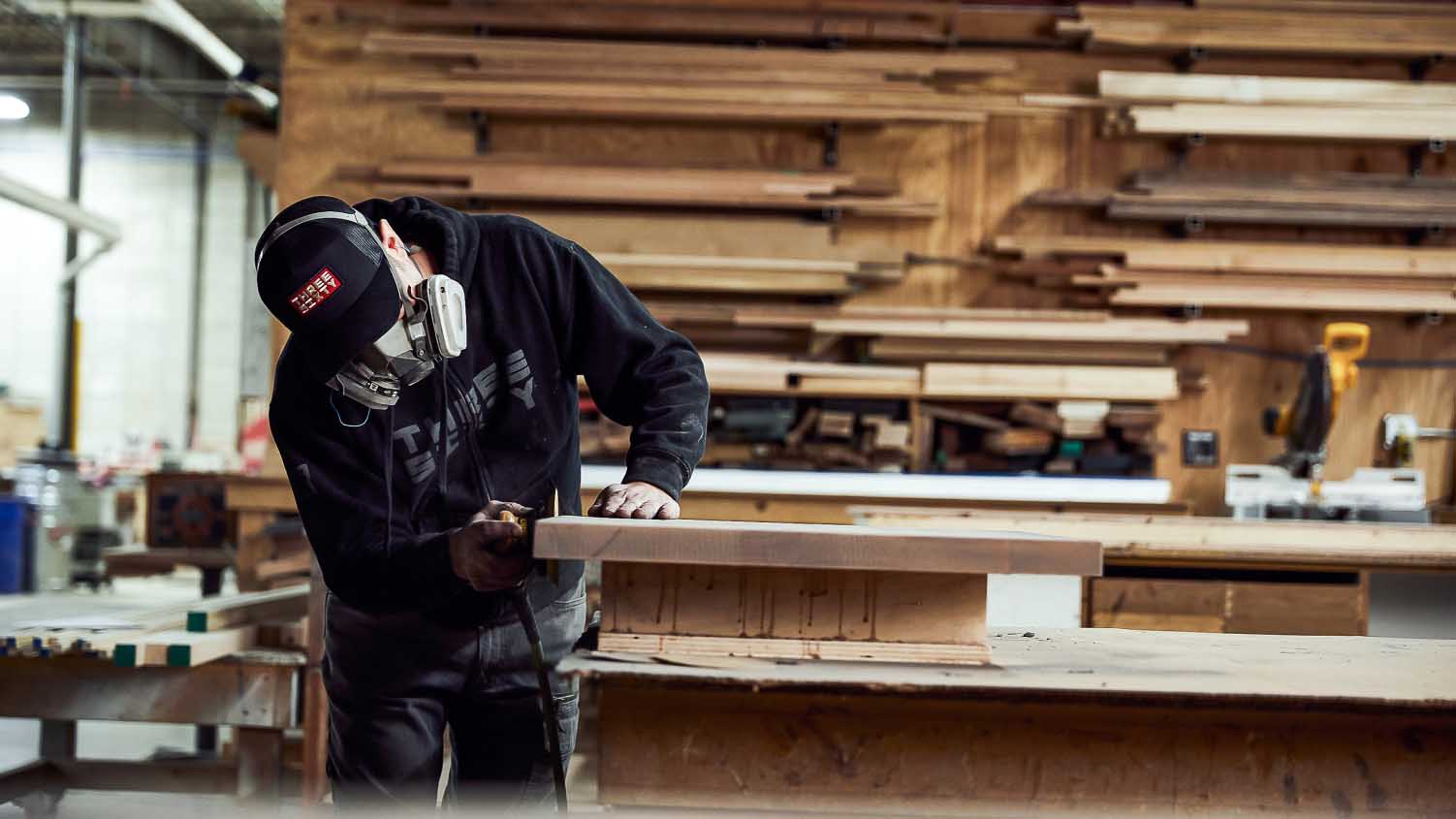 worker wearing a respiratory mask working with wood in a fabrication shop