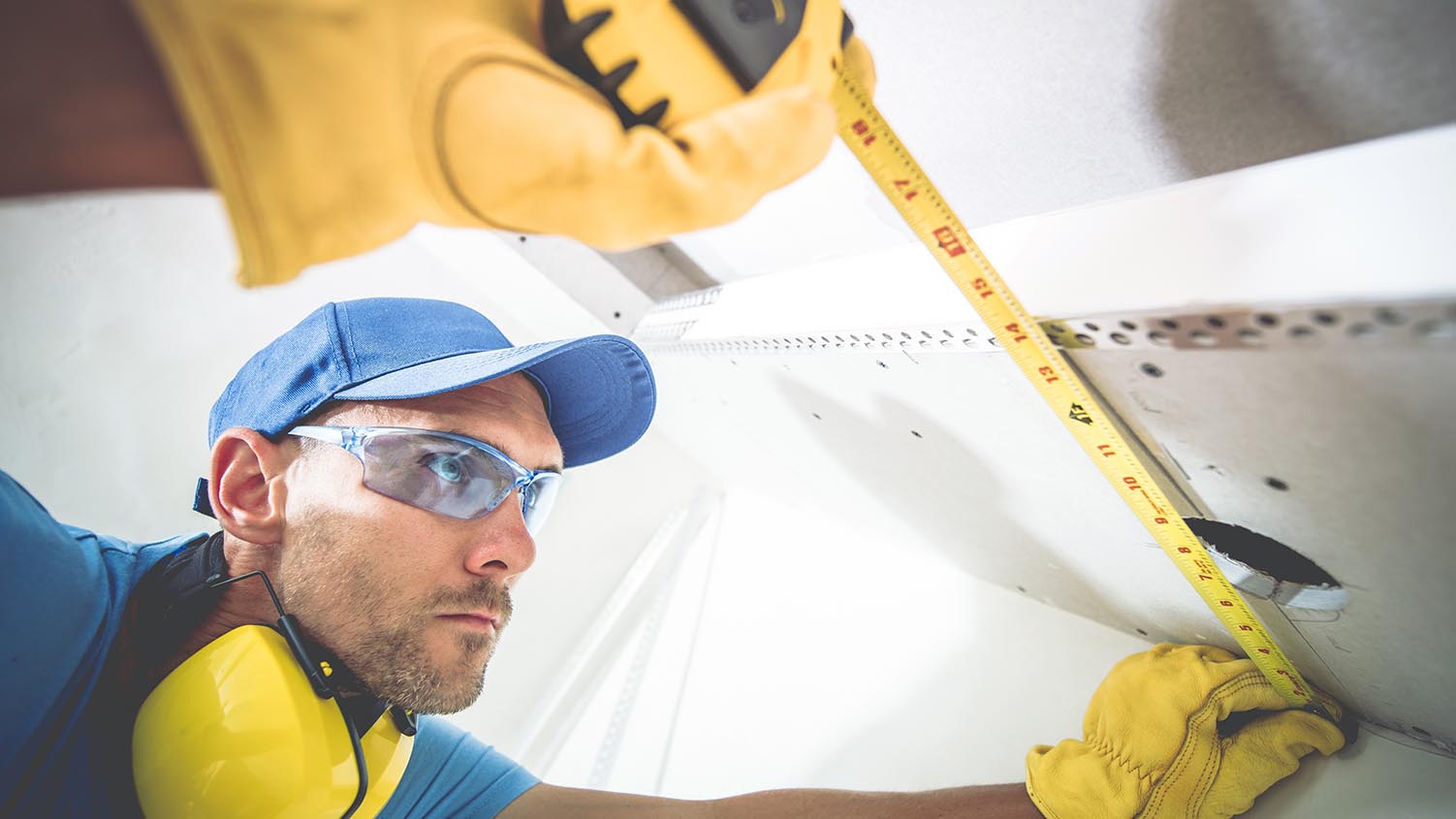 image of a worker wearing safety glasses, hearing protection, and safety gloves using a measuring tape