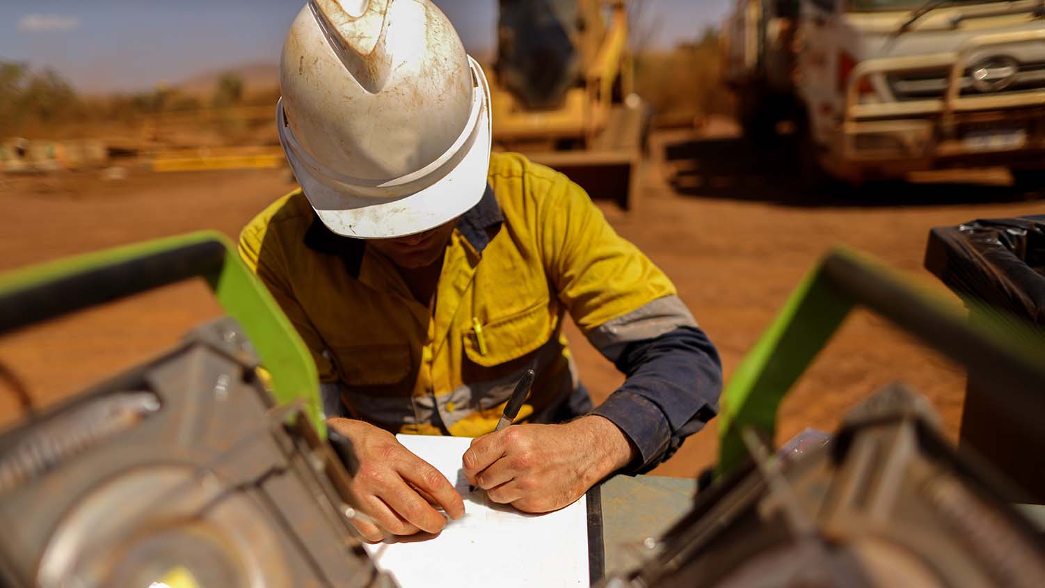 image shows a worker at a jobsite wearing a hard hat and writing on a clipboard
