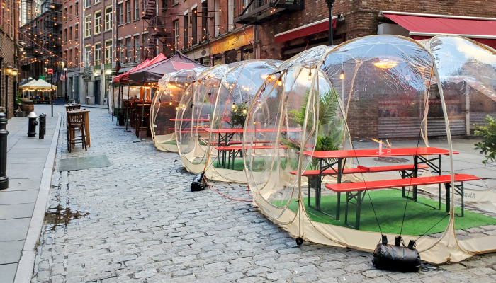 Outdoor dining 'tents' lined up outside a restaurant on a cobblestone street.